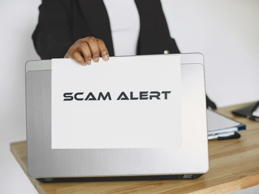 Cartel de alerta de estafa sobre ordenador portátil, representando las señales de alerta antes de contratar una agencia de OnlyFans en España